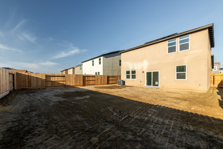 A dirt road with a fence and buildings on the side.