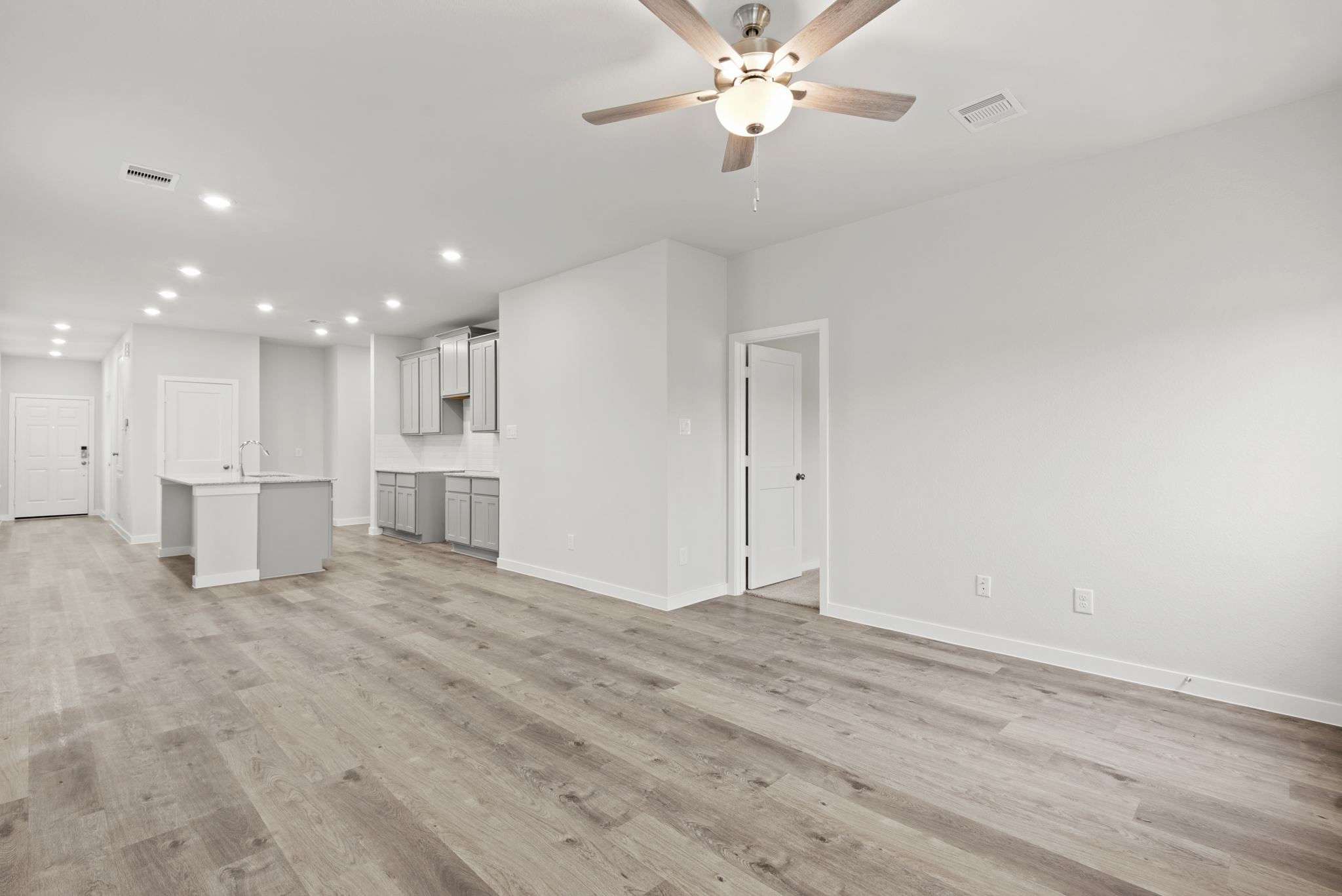 A large empty room with a ceiling fan and white cabinets.