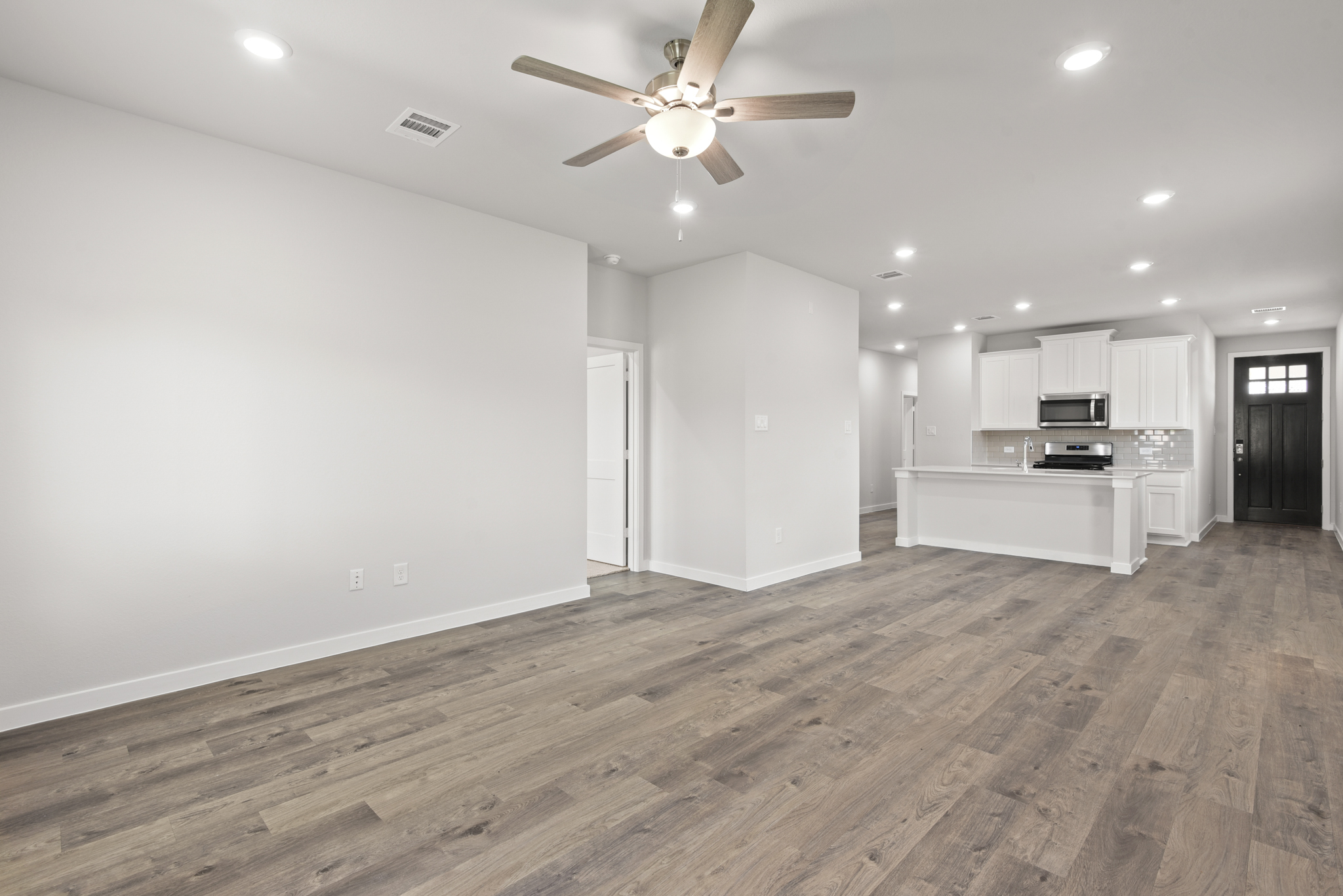 A large empty room with a ceiling fan and a wood floor.